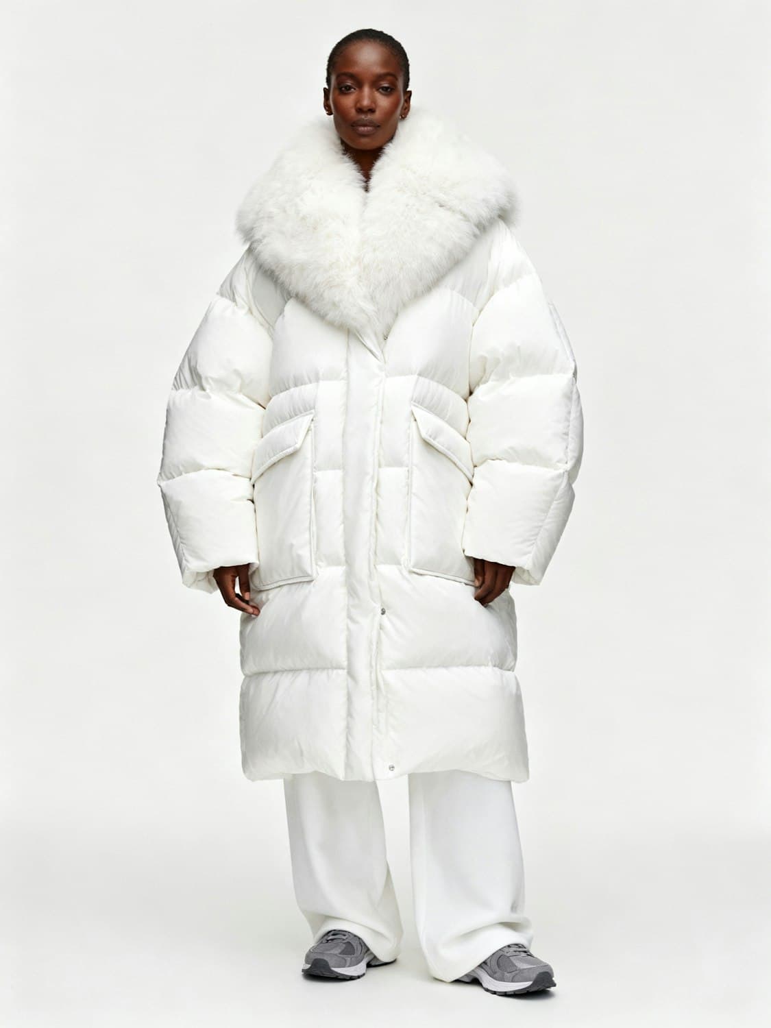 Woman in an oversized white puffer coat with a fur collar and wide white trousers